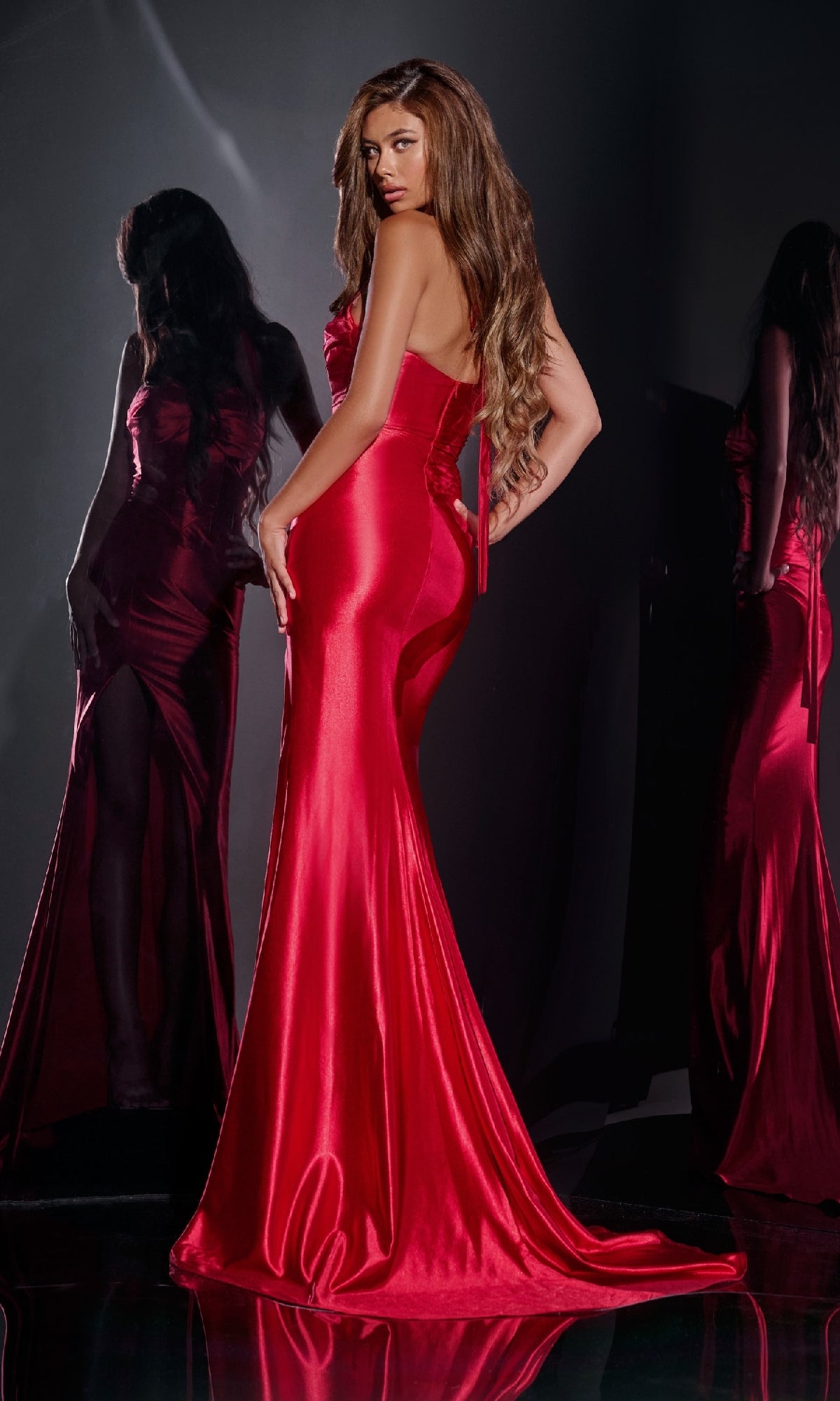 A woman with long hair poses with her back turned, looking over her shoulder, in the Jovani D5006 Deep V-Neck Long Halter Prom Dress; two reflections appear behind her.
